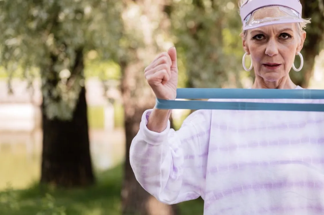 Older adult exercising with a resistance band in a green park. Illustrative stock photograph.