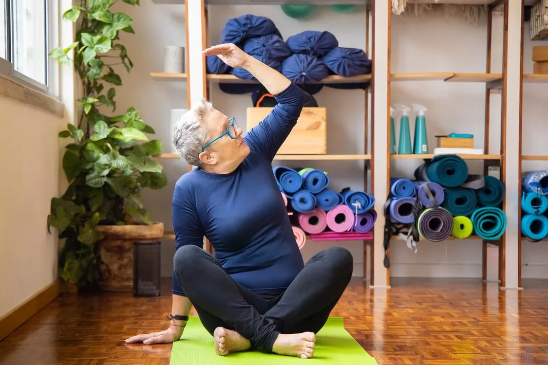 A woman practising yoga while seated on a green mat.