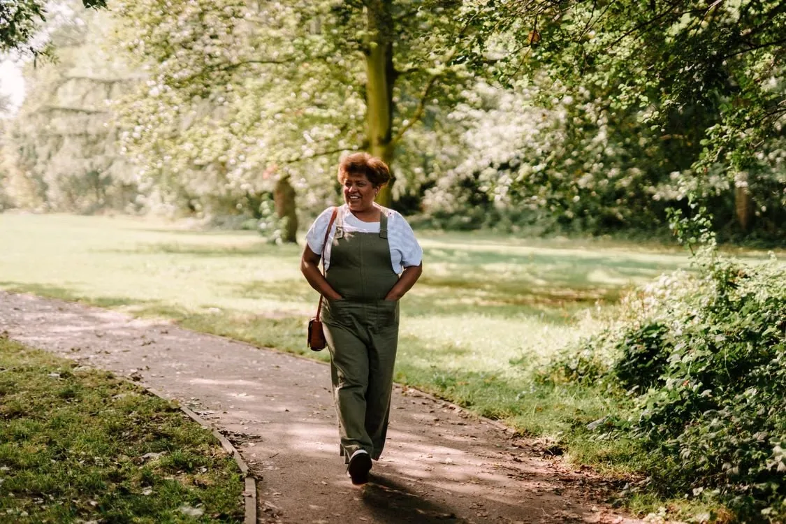 A woman walking along a sunlit path in a green park.
