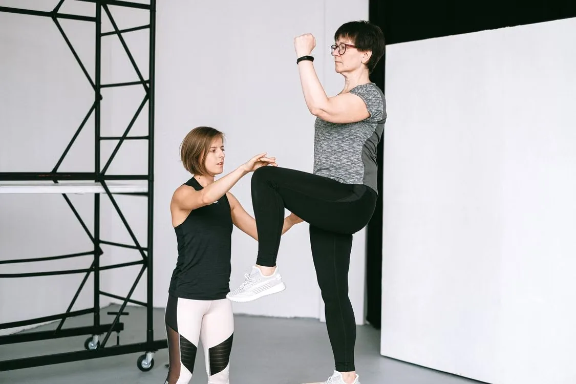 Two adults practising a standing balance exercise together.