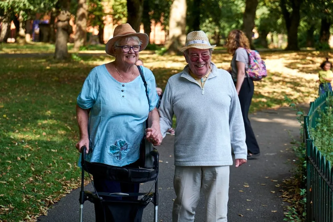 Two older adults walking together through a sunny park. Illustrative stock photograph.