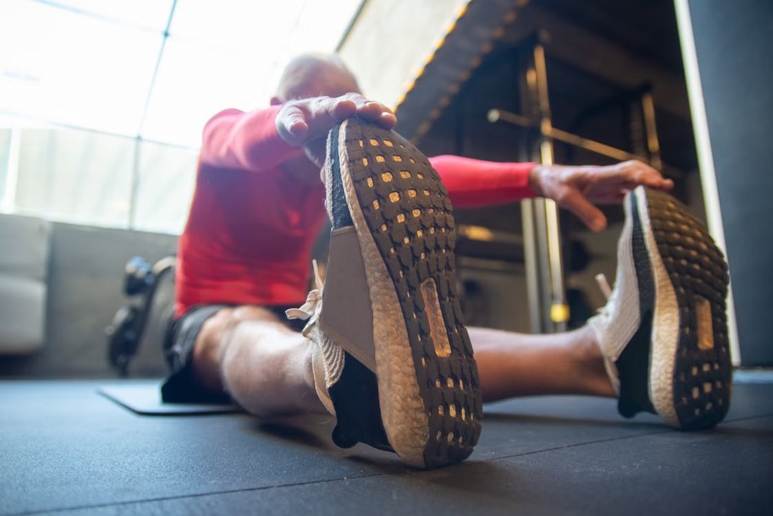 An older adult stretching while seated on an exercise mat.