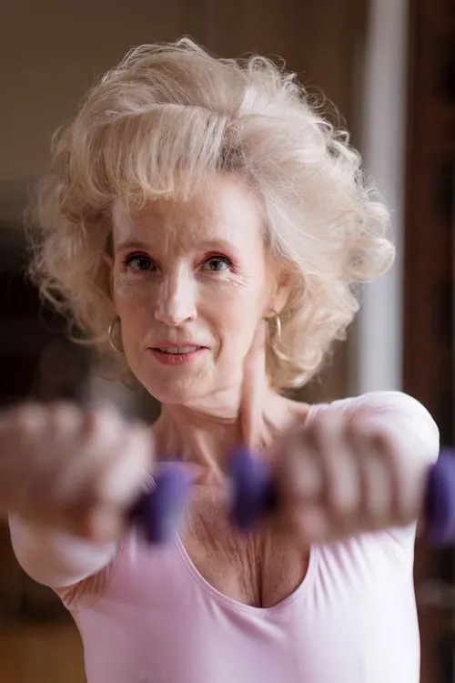 An older woman holding dumbbells during an indoor exercise session.
